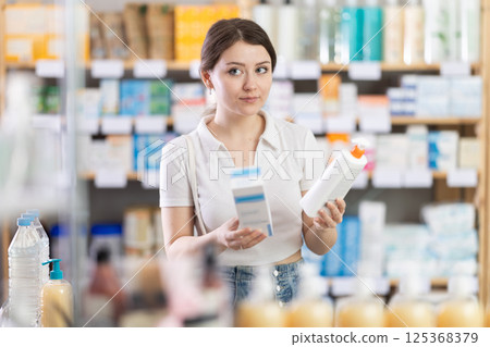 Girl in summer clothes choosing skin cream at drugstore 125368379