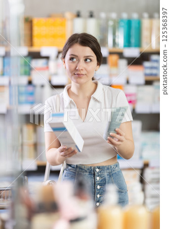 Girl in summer clothes choosing skin cream at drugstore Girl in summer clothes choosing skin cream at drugstore 125368397