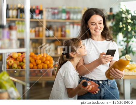 Girl with mother customers at shop scans QR code on juice package using phone camera Girl with mother customers at shop scans QR code on juice package using phone camera 125368400