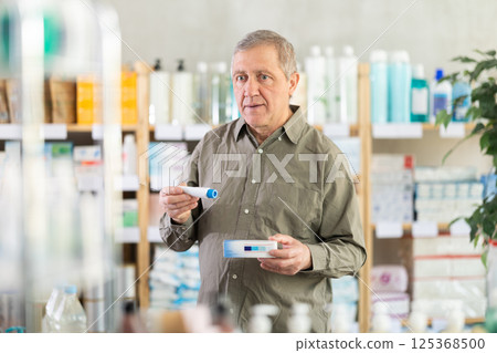 Older man examining box of ointment in pharmacy 125368500