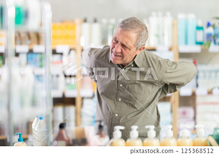 Senior man suffering from back pain while looking for medicine at drugstore 125368512