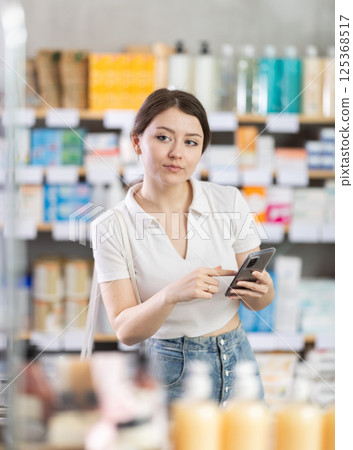 Girl checking list of needed items on phone while shopping at drugstore 125368517
