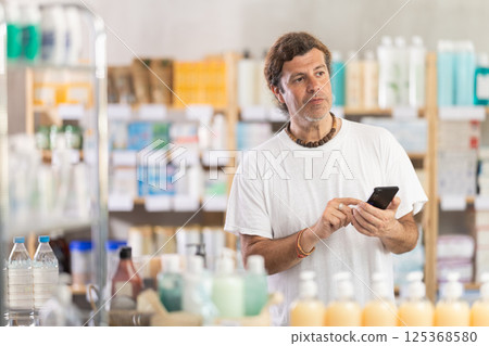 Adult man with phone choosing medicines and hygiene products 125368580