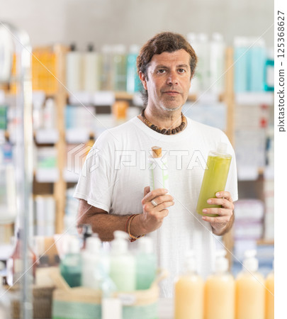 Adult man chooses shampoo or shower gel at pharmacy Adult man chooses shampoo or shower gel at pharmacy 125368627