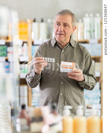 Elderly man in a pharmacy chooses pills Elderly man in a pharmacy chooses pills 125368647