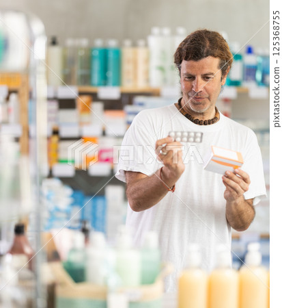 adult man chooses a package of pills in a pharmacy 125368755