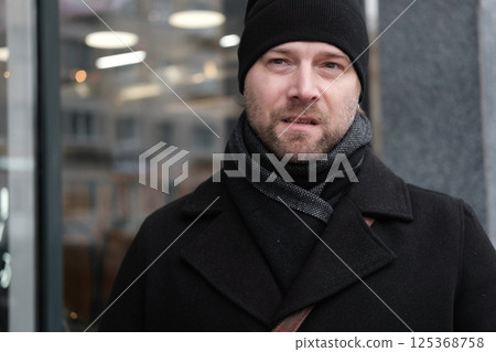 Handsome man wearing black coat and brown leather bag walking down on the city with mobile phone in hand. Stylish bearded middle-aged male using smartphone at urban street. Businessman going on job. Handsome man wearing black coat and brown leather bag walking down on the city with mobile phone in hand. Stylish bearded middle-aged male using smartphone at urban street. Businessman going on job. 125368758