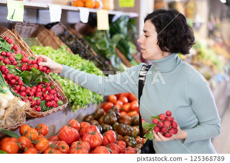 Portrait of female shopper choosing tomatoes at supermarket counter 125368789
