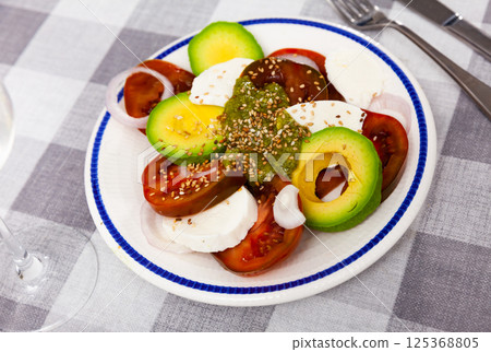 Portion of traditional Italian salad, caprese with avocado 125368805