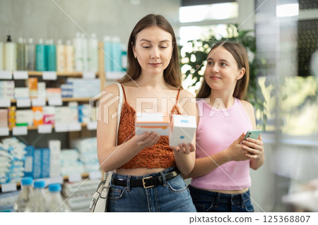 young woman with her daughter choosing pills at the pharmacy 125368807