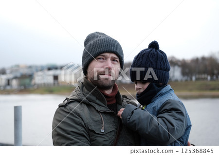 Father and son walking down on sidewalk together. Portrait of a handsome middle-aged man with toddler boy in the urban street. Dad and his child sitting on a bench in city park. City life. Family Father and son walking down on sidewalk together. Portrait of a handsome middle-aged man with toddler boy in the urban street. Dad and his child sitting on a bench in city park. City life. Family 125368845
