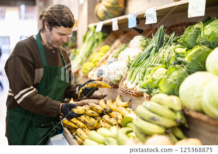 Adult man seller puts bananas on display 125368875