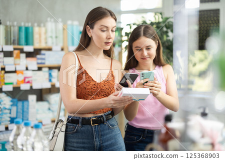Daughter and mother in summer clothes scans code on pills to check expiration date 125368903