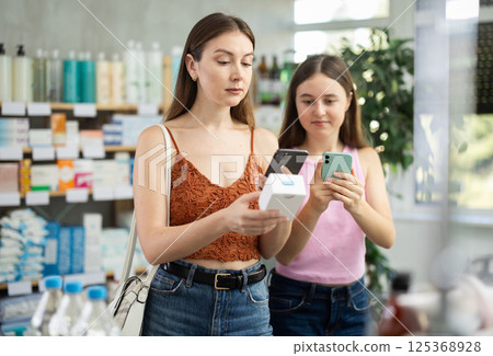 Daughter and mother in summer clothes scans code on pills to check expiration date 125368928