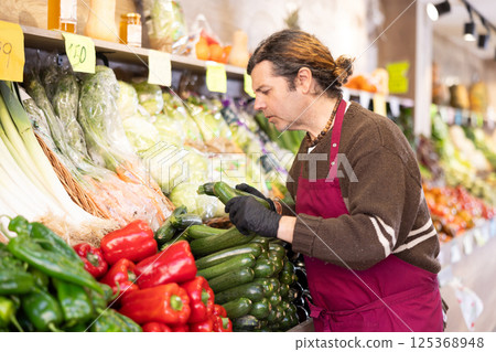 Man shop seller puts zucchini goods on display case 125368948