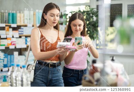 Near display case in pharmacy, mom with daughter scans barcode on paracetamol tablet 125368991