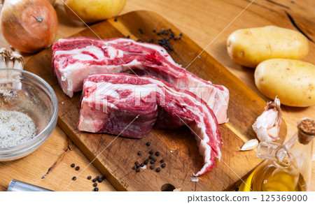 Raw beef ribs on board, potato tubers and whole onions Raw beef ribs on board, potato tubers and whole onions 125369000