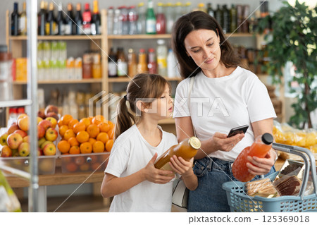 Girl with mother customers at shop scans QR code on juice package using phone camera Girl with mother customers at shop scans QR code on juice package using phone camera 125369018