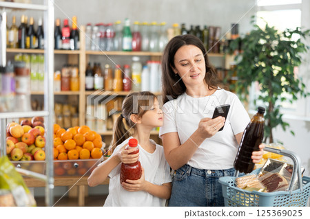 Girl with mother customers at shop scans QR code on juice package using phone camera 125369025