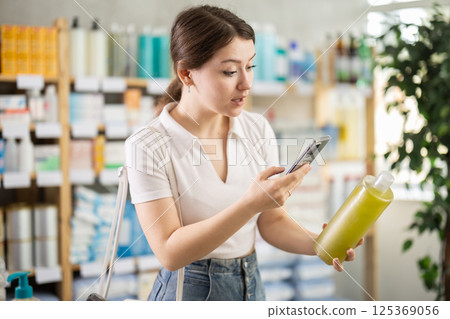 Girl in summer clothes scans code on medicinal shampoo to check expiration date 125369056