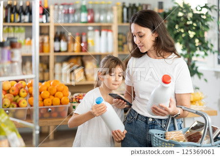 Girl with mother customers at shop scans QR code on milk package using phone camera 125369061