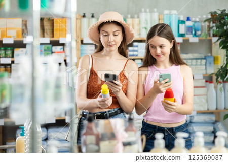 Daughter and mother in summer clothes scans code on sunscreen to check expiration date Daughter and mother in summer clothes scans code on sunscreen to check expiration date 125369087