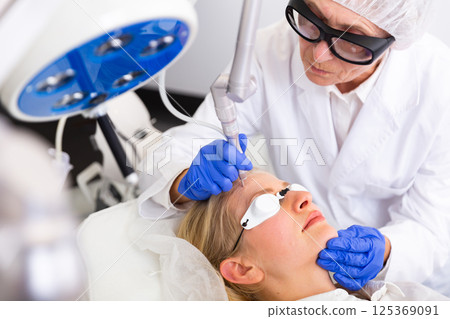 Cosmetologist doing laser wart removal procedure for young woman Cosmetologist doing laser wart removal procedure for young woman 125369091