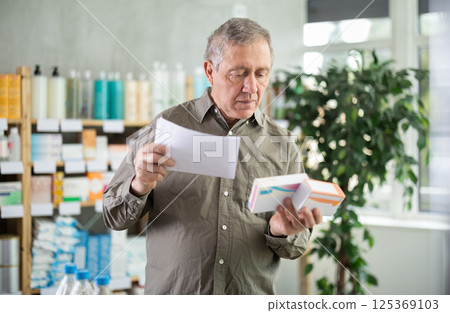 Elderly man comparing medications to prescription at pharmacy 125369103