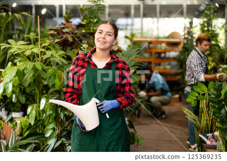 Young florist woman poses with a watering can in her hands Young florist woman poses with a watering can in her hands 125369235