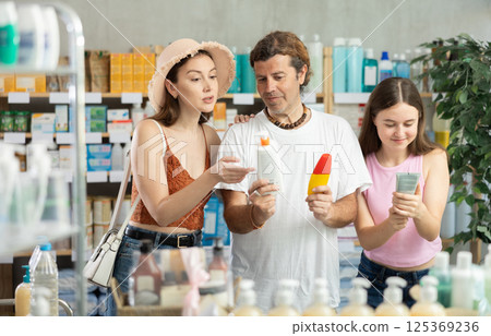 Woman with teen girl and husband are busy choosing sunscreen cream at pharmacy Woman with teen girl and husband are busy choosing sunscreen cream at pharmacy 125369236