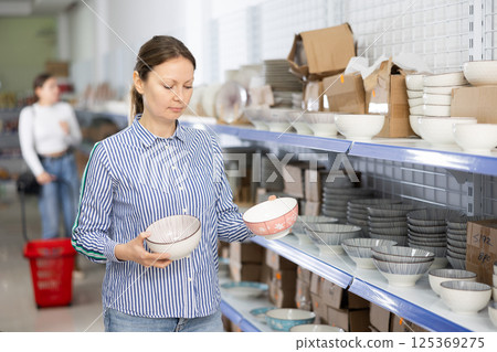 Female shopper choosing ceramic bowls on shelves at Asian store 125369275
