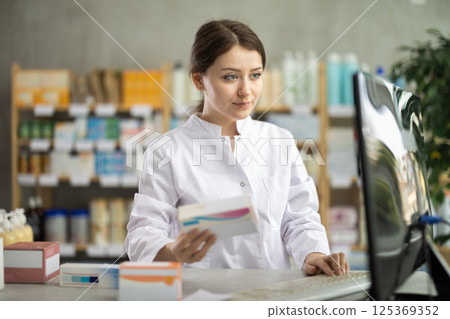 Female pharmacist updating stock inventory on pharmacy computer 125369352