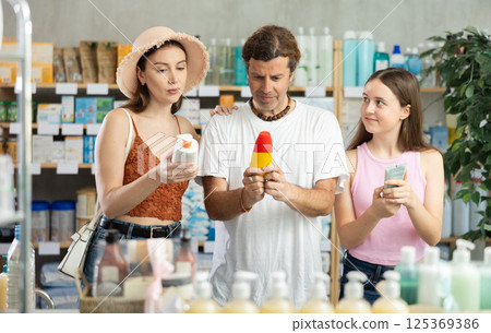 Father, mother and daughter choose sunscreen together at drugstore Father, mother and daughter choose sunscreen together at drugstore 125369386