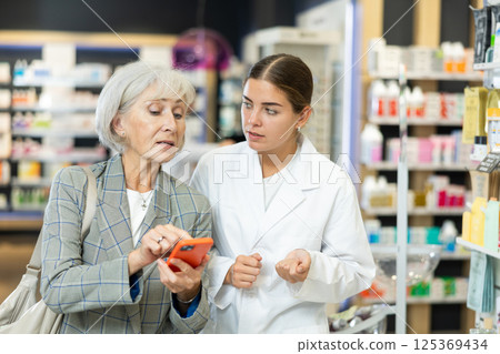 Old female customer asking young chemist about product reflected on her phone Old female customer asking young chemist about product reflected on her phone 125369434