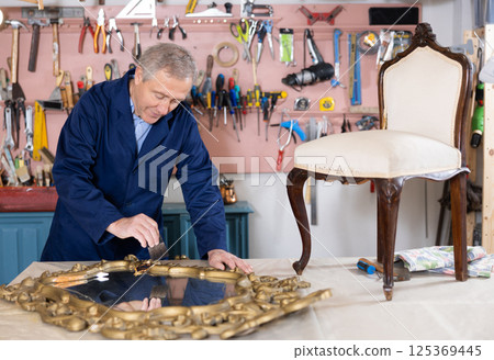 restorer carefully covers carved wooden frame of antique wall mirror with layer of varnish restorer carefully covers carved wooden frame of antique wall mirror with layer of varnish 125369445