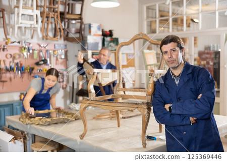 Portrait of middle-aged skillful repairman carpenter posing with crossed hands during workday in furniture woodwork studio Portrait of middle-aged skillful repairman carpenter posing with crossed hands during workday in furniture woodwork studio 125369446