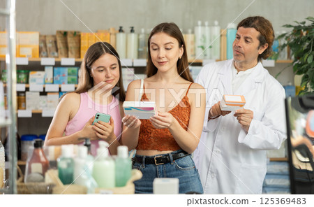 Mother and daughter choose pills in drugstore. Male pharmacist offers to buy pills Mother and daughter choose pills in drugstore. Male pharmacist offers to buy pills 125369483
