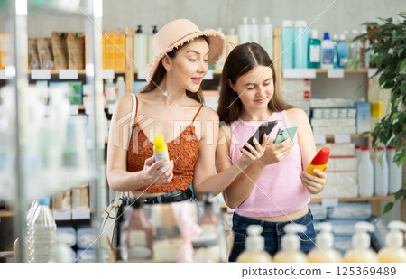 Daughter and mother in summer clothes scans code on sunscreen to check expiration date 125369489
