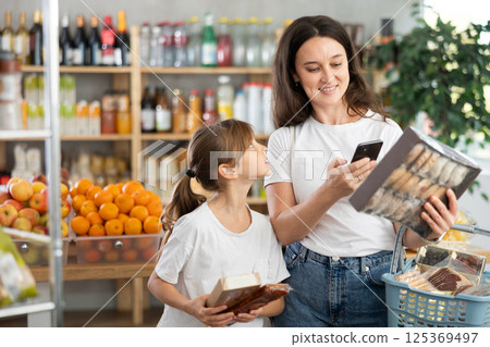 Daughter and mother choose delicious cookies in supermarket - scan QR code on label with smartphone 125369497