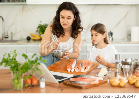 Happy mother and her daughter preparing salmon in the kitchen 125369547