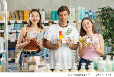 Man with wife and teen daughter customers in drugstore choose with different products Man with wife and teen daughter customers in drugstore choose with different products 125369551