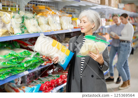 Interested mature female shopper choosing noodles at Asian store Interested mature female shopper choosing noodles at Asian store 125369564