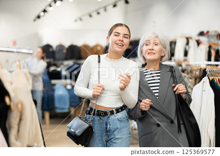 Two women customers watching large stock of clothes in clothing store Two women customers watching large stock of clothes in clothing store 125369577