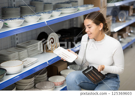 Young girl choosing square ceramic Asian style plates in store Young girl choosing square ceramic Asian style plates in store 125369603