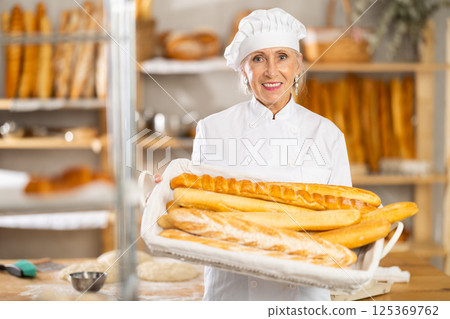 Senior female baker worker shows baguette 125369762