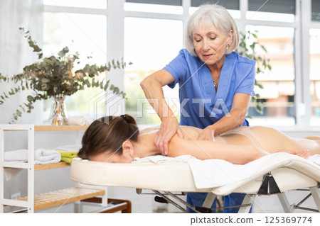 Unrecognizable young woman lies face down and enjoy shoulder massage for body care Unrecognizable young woman lies face down and enjoy shoulder massage for body care 125369774