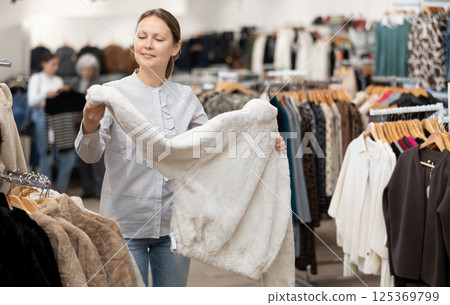 Middle-aged woman choosing short fur coat in clothing shop 125369799