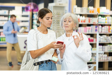 Senior female pharmacist talk to girl buyer and help to scan QR code on package 125369821