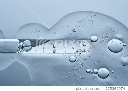 The texture of the facial serum with bubbles and an eyedropper on a blue background. The texture of the facial serum with bubbles and an eyedropper on a blue background. 125369974