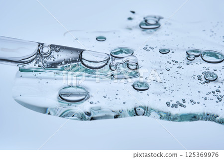 A puddle of transparent serum with microneedles on a blue background. A puddle of transparent serum with microneedles on a blue background. 125369976